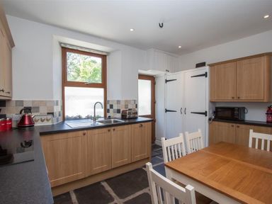 A kitchen with wooden cabinets a wooden table and white chairs a window above the sink a microwave and toaster on countertops at Robins Nest in Coniston