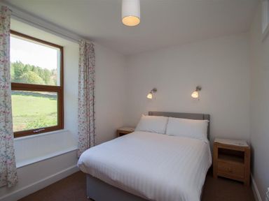 A bedroom with a double bed two bedside tables and a window with curtains at Robins Nest in Coniston