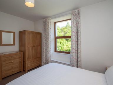 A bedroom with a bed dresser wardrobe mirror and window with curtains at Robins Nest in Coniston