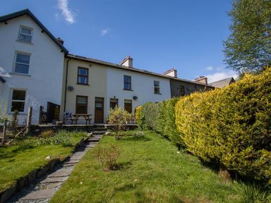 A garden with a stone path leading to a row of houses with a picnic table and trimmed hedges at Robins Nest in Coniston