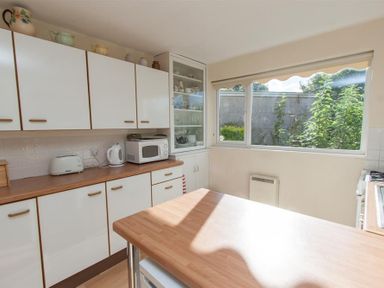 A kitchen with white cabinets a microwave kettle toaster and a window showing outdoor plants at Brimbles in Keswick