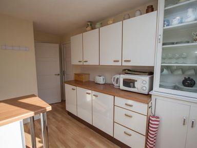 A kitchen with white cabinets a wooden countertop a microwave kettle toaster and a glass cupboard with dishes and cups at Brimbles Keswick
