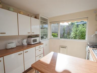 A kitchen with white cabinets a microwave toaster and kettle on the countertop and a window showing plants outside at Brimbles in Keswick
