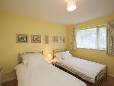 A bedroom with two single beds a bedside table lamp and framed pictures on a yellow wall at Brimbles in Keswick
