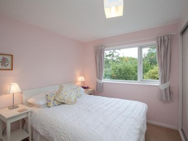 A bedroom with a double bed lamps bedside tables window with curtains and garden view at Brimbles in Keswick