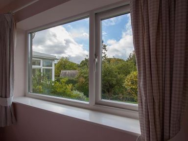 A window with checked curtains looking out to trees and a cloudy sky at Brimbles in Keswick