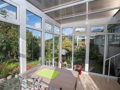 A conservatory with a dining table and chairs and a lamp next to the windows at Brimbles in Keswick
