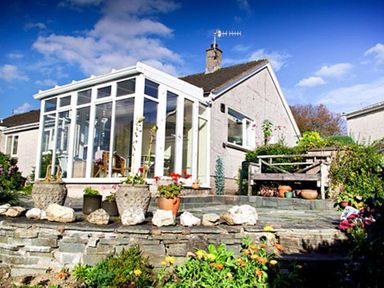 A house with a glass conservatory surrounded by a stone patio and garden at Brimbles in Keswick