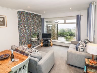 A living room with grey sofas a wooden table a tv and large window at Helm Crag in Grasmere