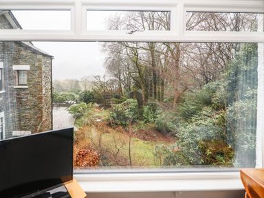 A window view showing a stone building patio and garden area with trees and bushes at Helm Crag in Grasmere