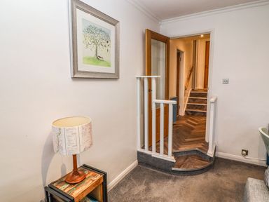 A hallway with a small wooden table with a lamp a framed tree picture on the wall and stairs leading to another room at Helm Crag in Grasmere