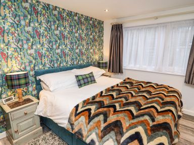 A bedroom with a double bed with white sheets and a patterned blanket next to two bedside tables with lamps and a window with curtains at Helm Crag in Grasmere
