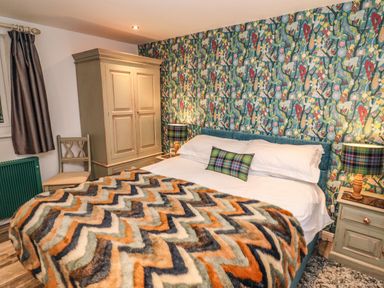 A bedroom with a bed with patterned blanket and pillow a wardrobe a chair and bedside tables with lamps at Helm Crag in Grasmere