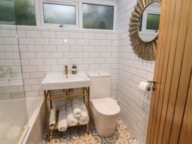 A small bathroom with a sink, toilet, mirror, towels on a rack, and patterned floor tiles at Helm Crag in Grasmere