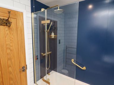 A bathroom with a glass shower screen bathtub and gold shower fixtures at Helm Crag in Grasmere