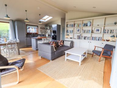An open plan living area with a grey sofa a white coffee table a dining table and chairs a kitchen with grey cabinets and a wall of bookshelves at How Beck in Hawkshead