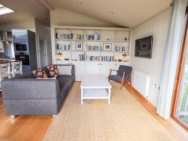 A living room with a gray sofa, armchair, white coffee table, bookshelf, and wall-mounted television at How Beck in Hawkshead