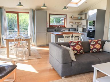An open plan living area with a gray sofa and patterned cushions a dining table with white chairs and tableware a kitchen with gray cabinets and wooden countertops at How Beck in Hawkshead