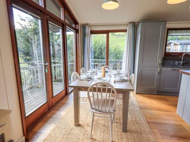 A dining area with a table set for six and large windows overlooking greenery at How Beck in Hawkshead