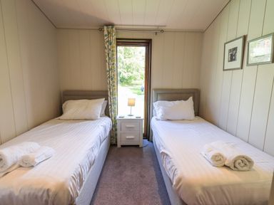 A bedroom with two single beds and a nightstand with a lamp by a window at How Beck in Hawkshead