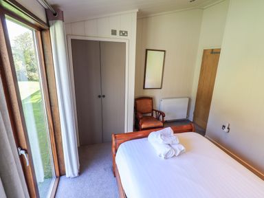 A bedroom with a wooden bed with white linens and towels a wooden chair a wall mirror and a wardrobe with sliding doors at How Beck Hawkshead