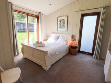 A bedroom with a double bed bedside tables lamps a chair sliding glass door and a frosted glass door at How Beck in Hawkshead