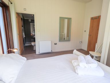 A bedroom with a bed with folded towels a mirror a chair and an open door to a bathroom at How Beck in Hawkshead