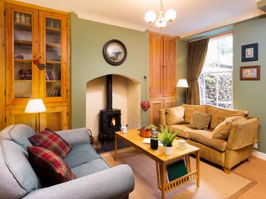 A living room with two sofas wood burning stove coffee table and built in cupboards at Greystones in Bowness