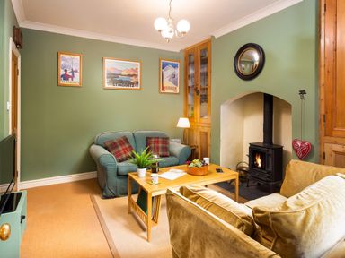 A living room with two sofas a wooden coffee table a wood burning stove and framed pictures on the walls at Greystones in Bowness