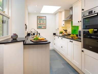 A kitchen with white cabinets black countertops a cutting board with vegetables a built in oven and a green backsplash at Greystones in Bowness