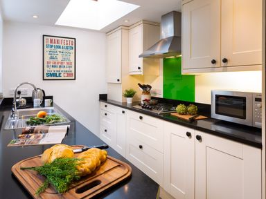 A kitchen with white cabinets black countertops a microwave stove a sink with vegetables and bread on the counter and a manifesto poster on the wall at Greystones in Bowness