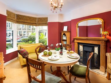 A dining room with a round table set for a meal a yellow sofa and a fireplace at Greystones in Bowness