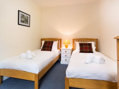 A bedroom with two single beds with wooden frames a nightstand with a lamp between the beds and a framed picture on the wall at Greystones in Bowness