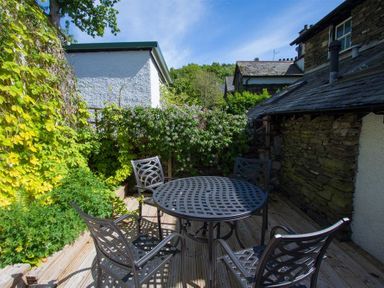 An outdoor patio with a round metal table and four metal chairs surrounded by plants and stone buildings at Greystones in Bowness