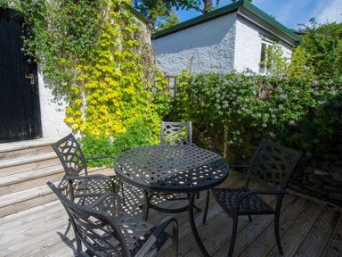 An outdoor patio with a round metal table and four matching chairs surrounded by plants and a white building at Greystones in Bowness