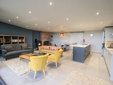 An open plan living room and kitchen with a gray sofa yellow chairs a glass coffee table a dining table and kitchen island at Gillside in Millbeck