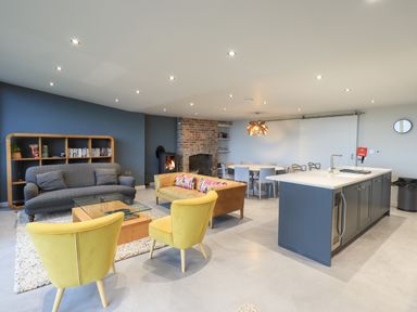 An open living room with yellow chairs a gray sofa a brown sofa a glass coffee table a wooden dining table a brick fireplace and a kitchen island at Gillside in Millbeck