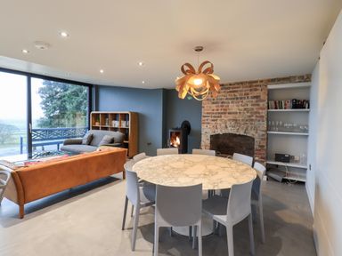 A dining area with a round marble table surrounded by gray chairs a brown couch a gray sofa a brick fireplace and large window at Gillside in Millbeck