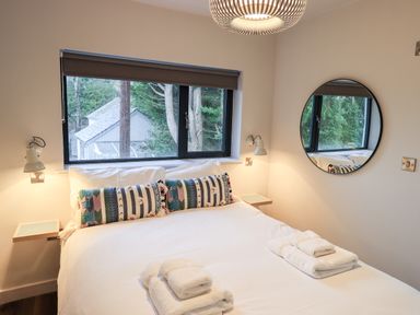 A bedroom with a double bed white linens colorful pillows round wall mirror and a window at Gillside in Millbeck