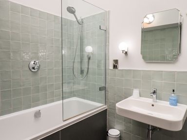 A bathroom with a bathtub shower combination and a sink with a mirror above at Gillside in Millbeck