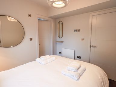 A bedroom with a bed with folded towels on it two doors a round mirror on the wall a light fixture and a small wall mirror at Gillside in Millbeck