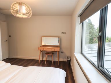 A bedroom with a bed, wooden dressing table with mirror and chair, large window, and ceiling light at Gillside in Millbeck