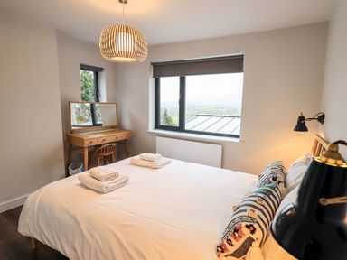 A bedroom with a bed, pillows, towels on the bed, a wooden desk with a mirror, and windows showing an outdoor view at Gillside in Millbeck