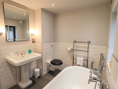 A bathroom with a pedestal sink mirror toilet with black seat towel rack and bathtub at Gillside Millbeck