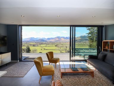 A living room with two yellow chairs a glass coffee table a dark sofa and a large window showing mountains at Gillside in Millbeck