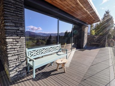 An outdoor deck with a wooden bench and small stool next to a building with large glass windows and stone walls at Gillside in Millbeck