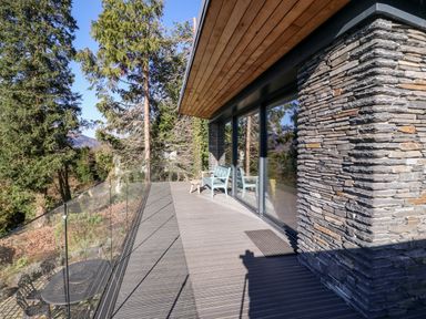 A balcony with glass railing a bench and a stool surrounded by trees at Gillside in Millbeck