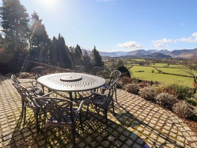 An outdoor patio with a round metal table and six chairs overlooking green fields and mountains at Gillside in Millbeck