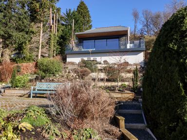 A garden with shrubs and a blue bench in front of a modern house with large glass windows at Gillside in Millbeck