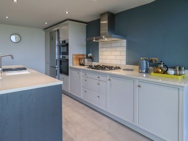 A kitchen with white cabinets a gas stove a stainless steel hood and a countertop with appliances at Gillside in Millbeck